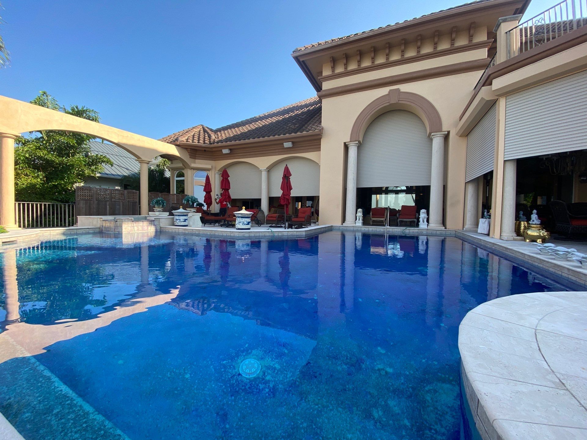 A Mediterranean-style pool home with roll-down shutters over its arched openings