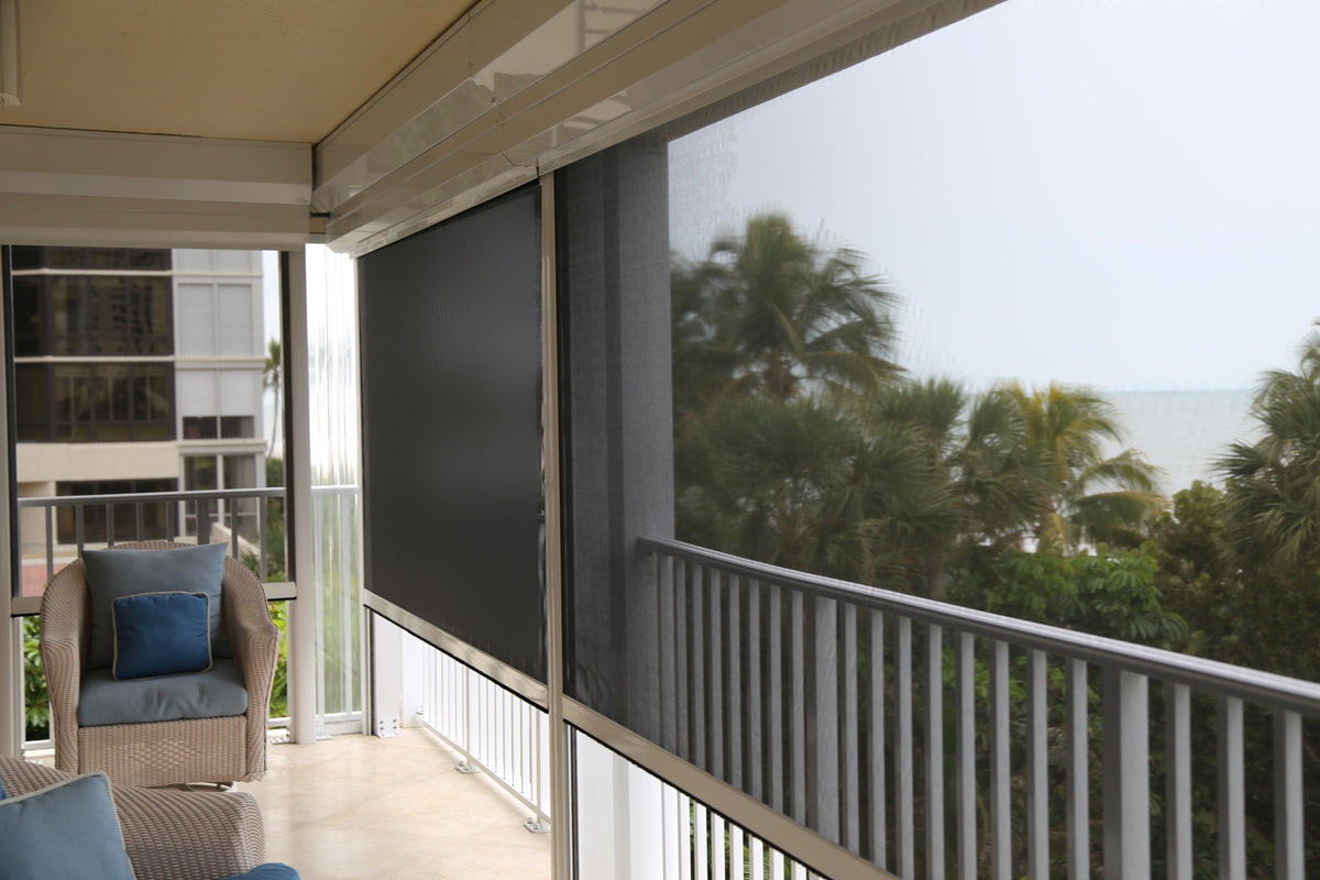 Dark retractable screens lowered from their housings on a condo balcony, with palms and the water behind