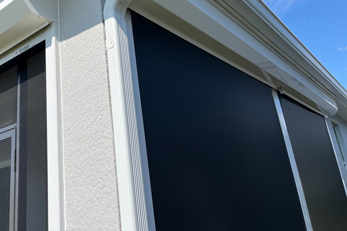 Black hurricane screens lowered flat across lanai openings on a white stucco house under a blue sky