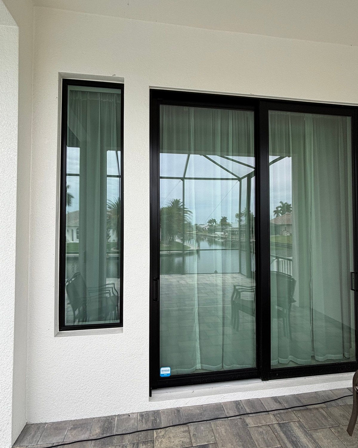 Black frame impact sliding glass door and tall side window on white stucco