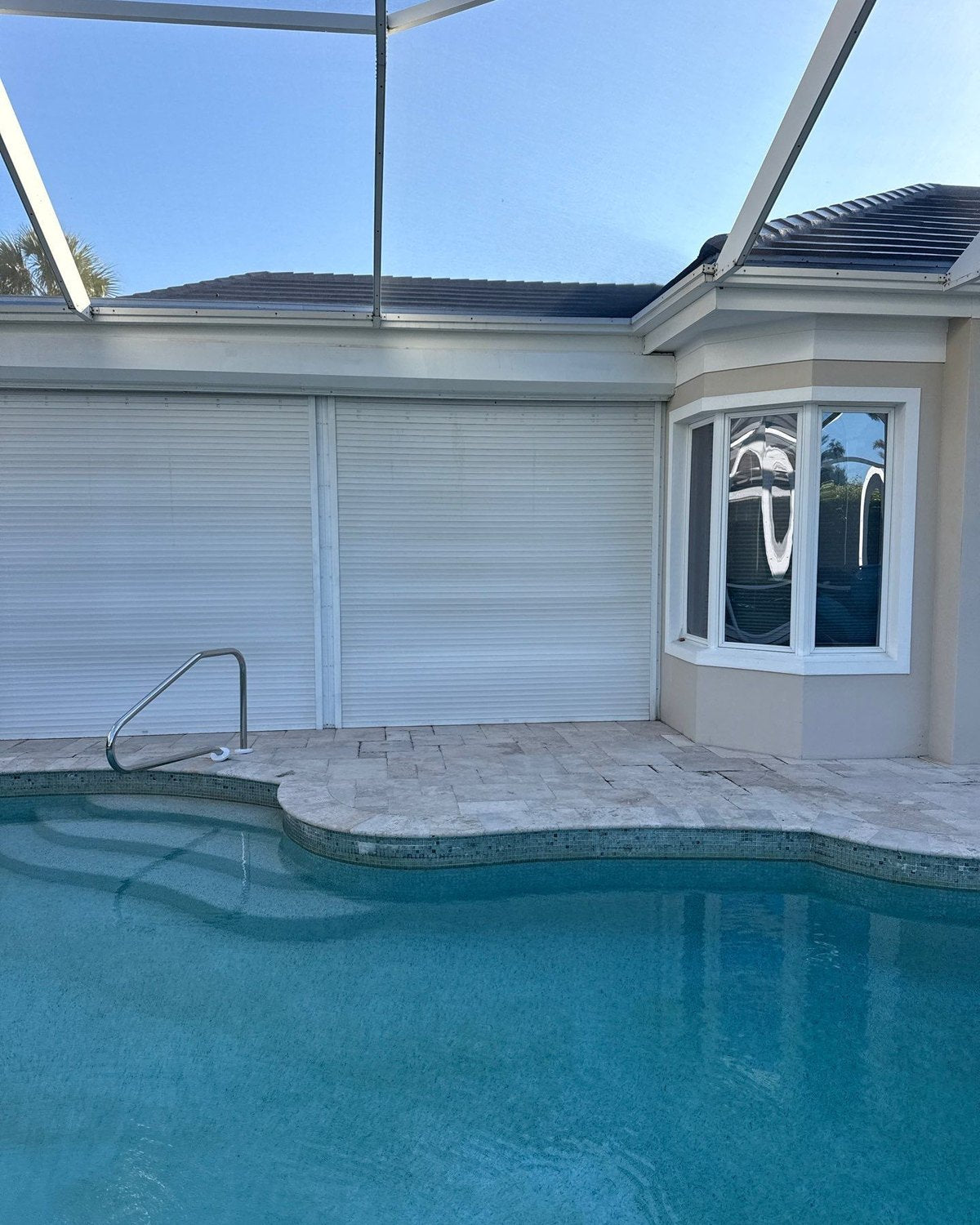 Two white roll-down shutters closed over lanai openings beside a pool