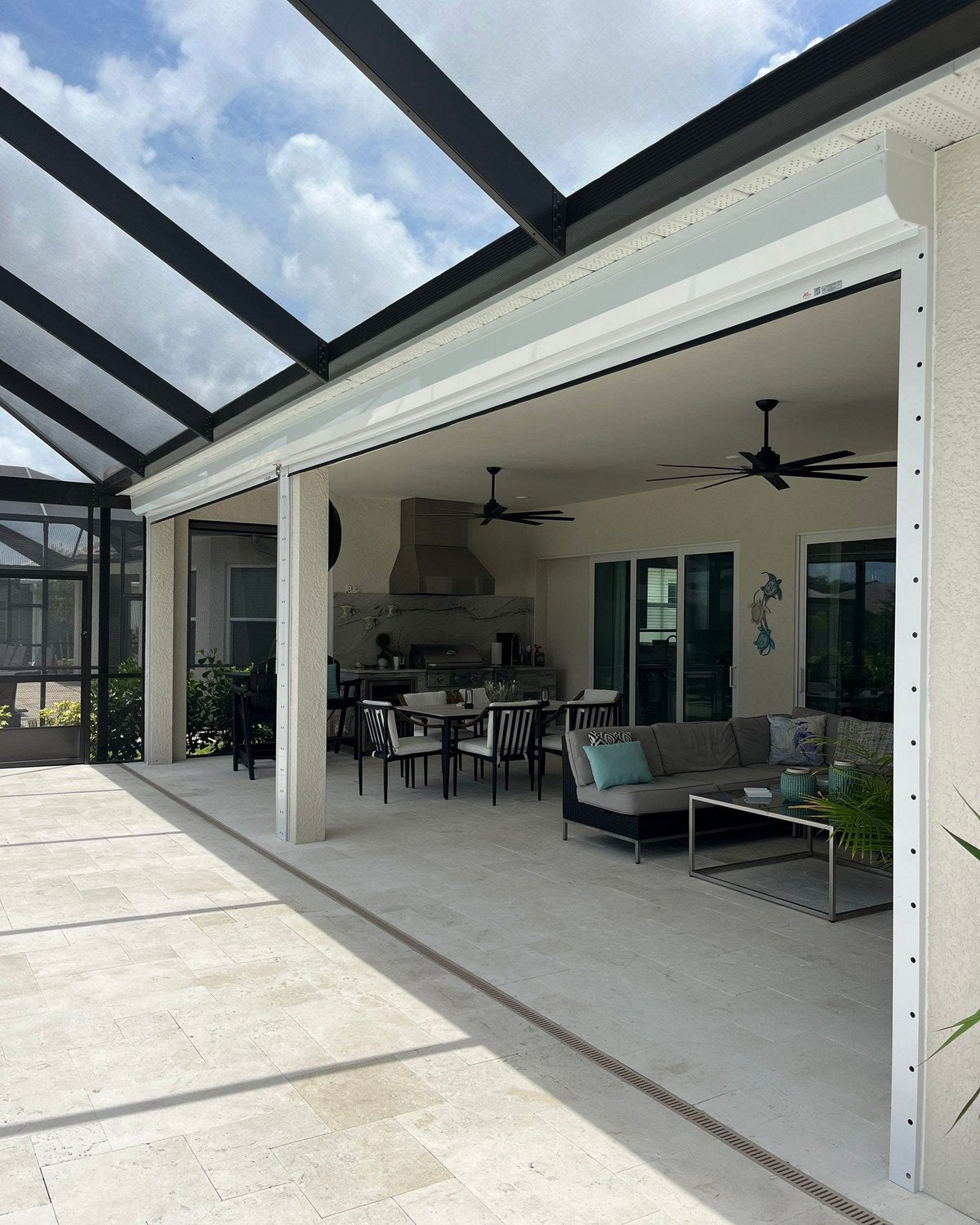 Covered lanai with the retractable screens rolled up into their housing, outdoor kitchen and seating inside