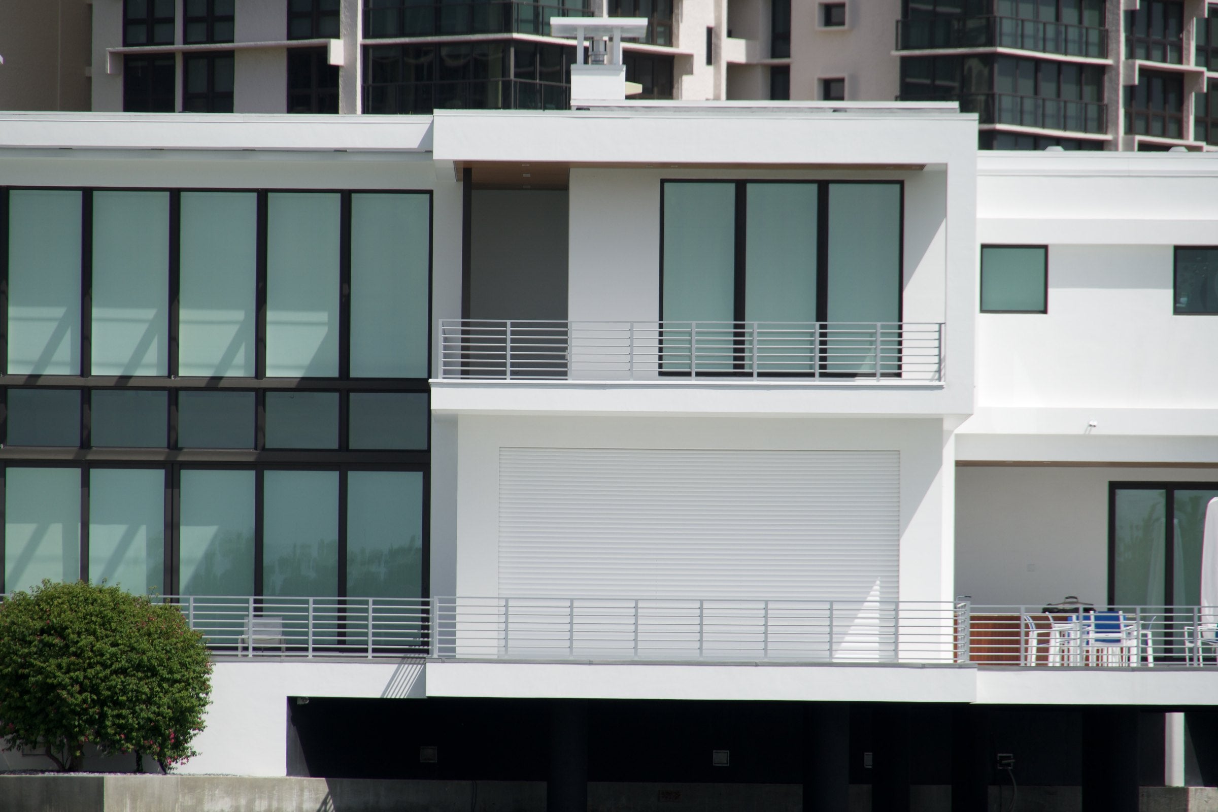 A modern white waterfront home with a closed AHT roll-down shutter on the ground floor