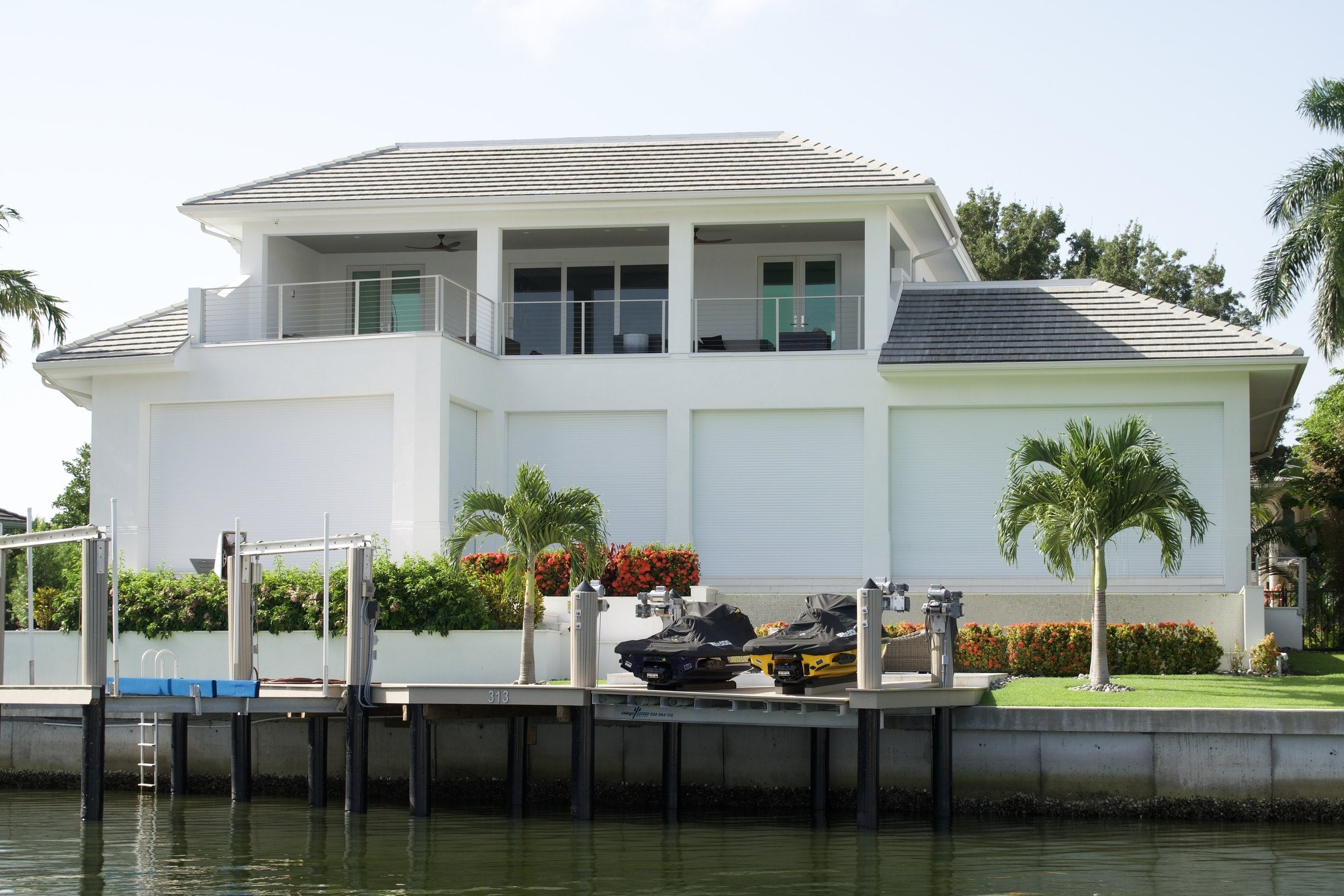 A waterfront Southwest Florida home with four closed AHT roll-down shutters across the ground floor